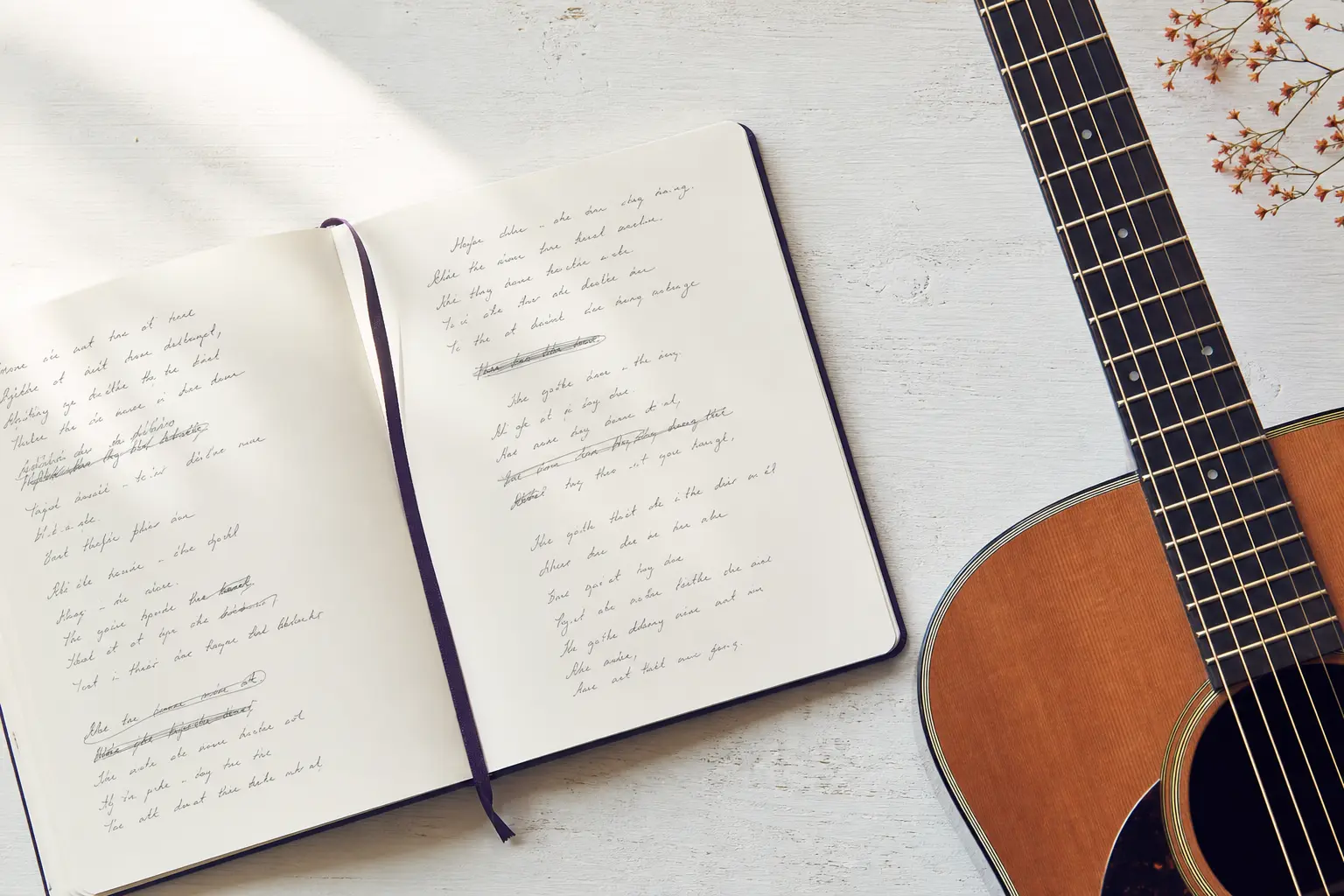 An open songwriter's notebook on a wooden desk beside an acoustic guitar, handwritten lyrics visible on the page